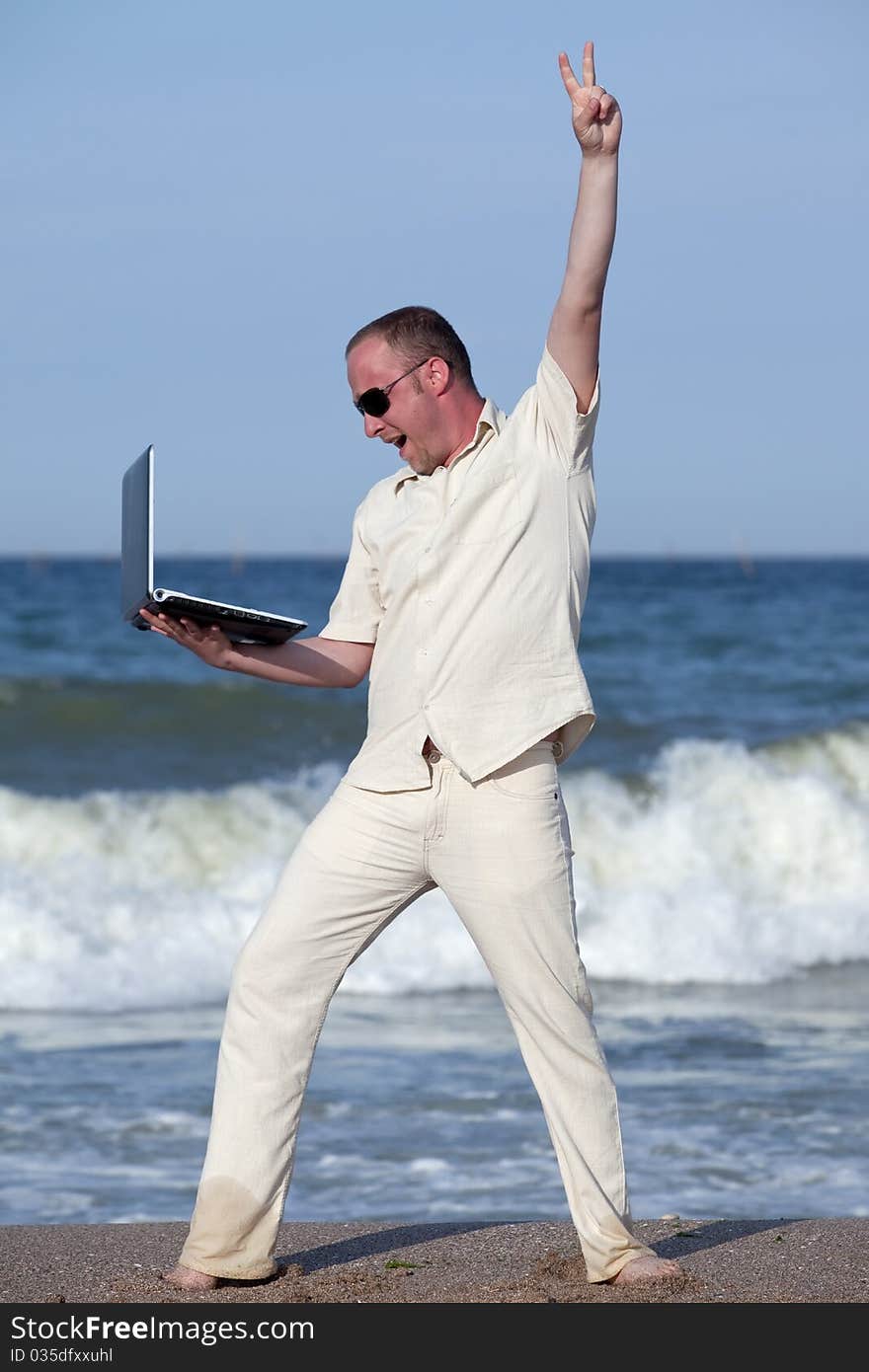 Young businessman at the beach with his laptop happy about success. Young businessman at the beach with his laptop happy about success