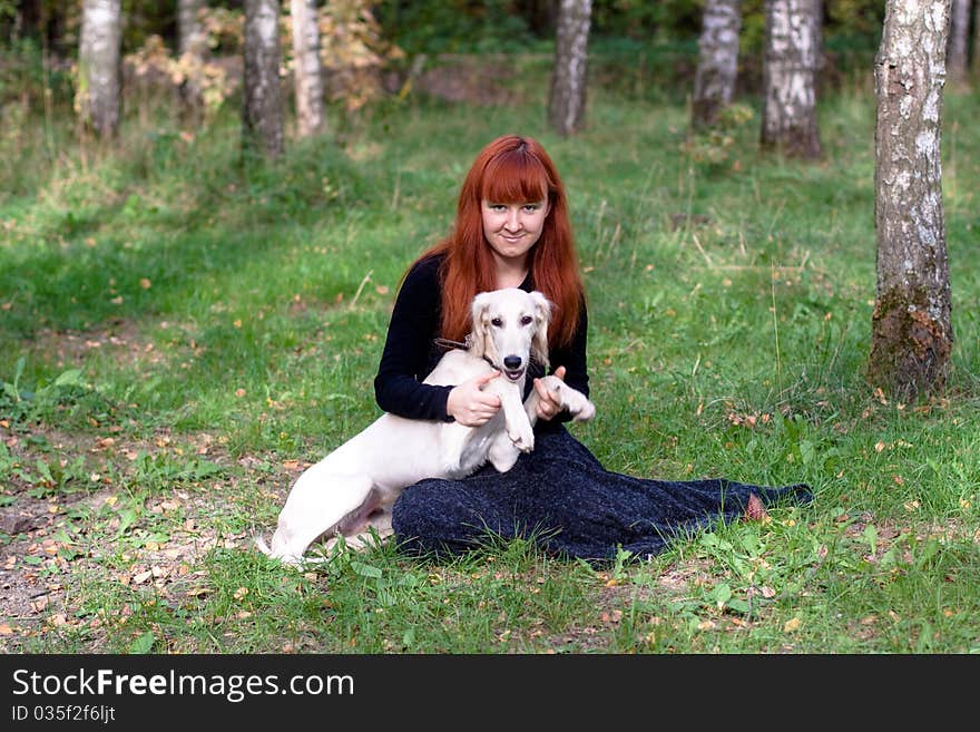 A girl in a black dress and white saliki pup in a forest. A girl in a black dress and white saliki pup in a forest