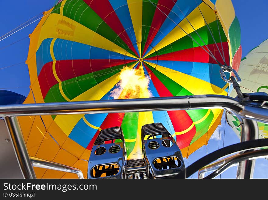 Photo of a colorful hot air balloon while he gets filled by flaming the air.
Two more balloons left and right.