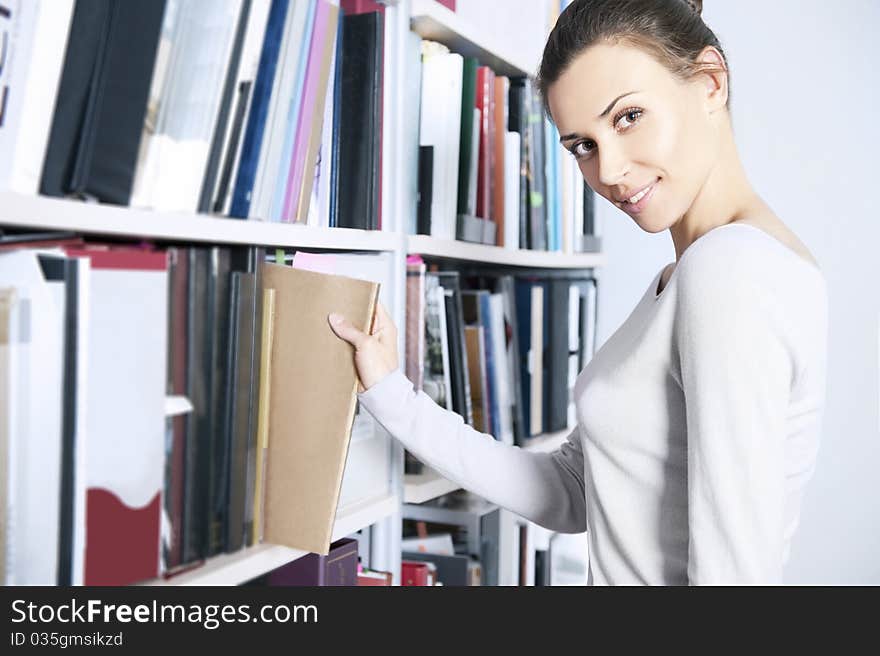 Young women stands near bookshelf