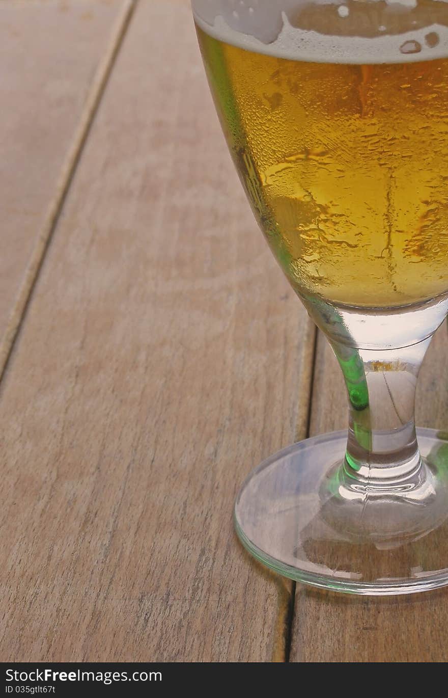 Glass of beer; closeup image of the beer in the elegant transparent glass, isolated on a wooden table, with space for text (copyspace) on the left side