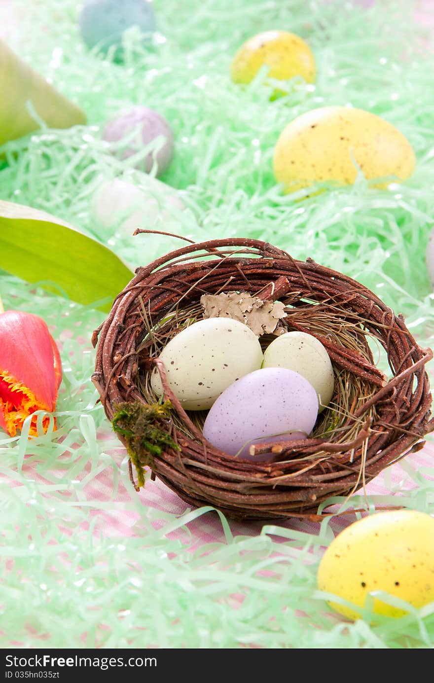 Colorful painted Easter eggs green, pink, yellow in birds nest decorated with spring tulips flowers on a pastel background