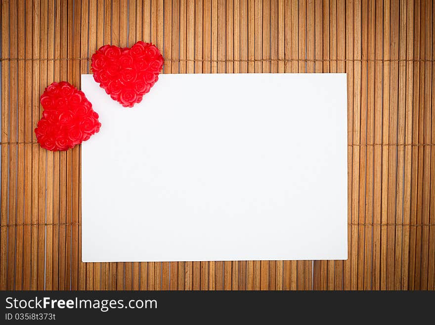 Two red hearts with paper card on wooden background