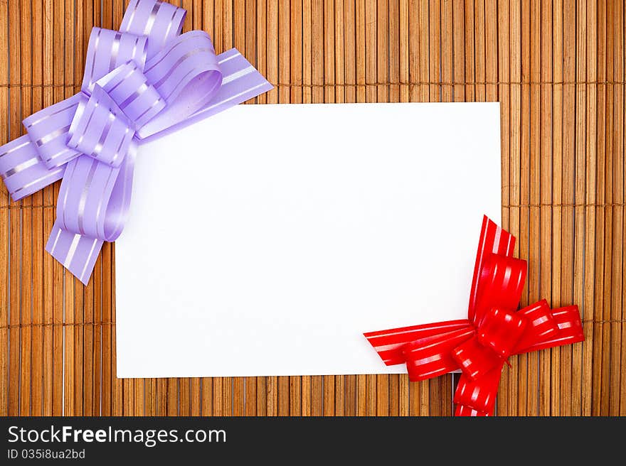 Violet and red bows with paper card on grunge wooden background