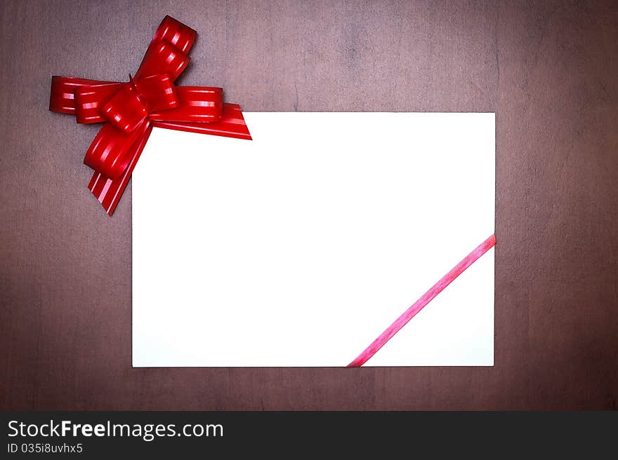 Red bow with paper card on grunge wooden background