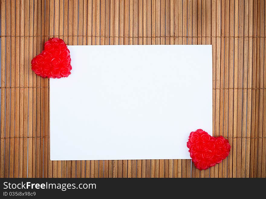 Two red hearts with paper card on wooden background