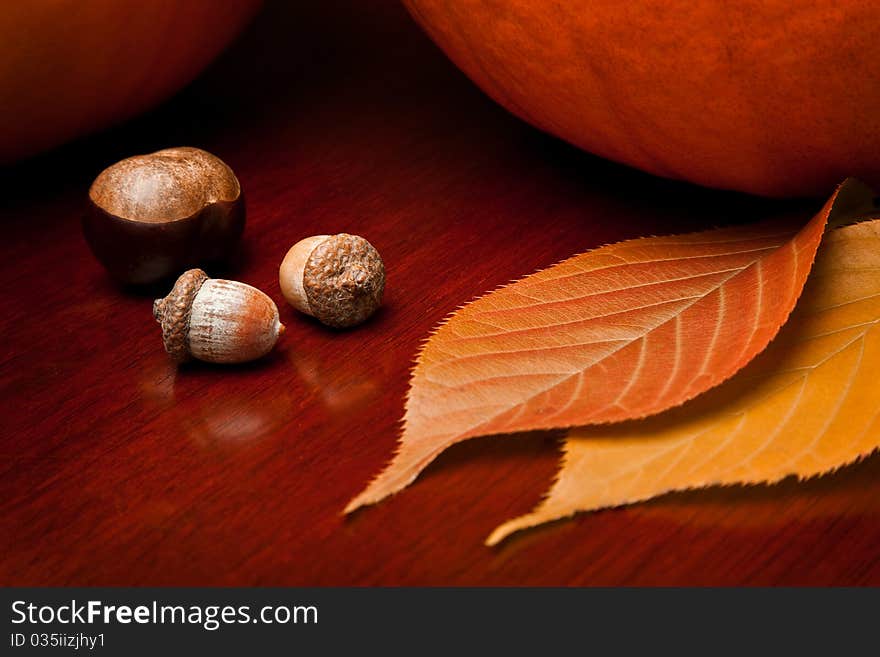 Two pumpkins, a chestnut, acorns and autumn leaves on a warm wooden table. Two pumpkins, a chestnut, acorns and autumn leaves on a warm wooden table.