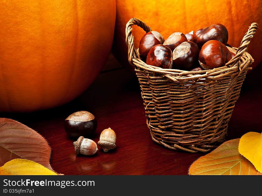 Two pumpkins, colored leaves, acorns, and a basket of chestnuts on a warm wooden tabletop. Two pumpkins, colored leaves, acorns, and a basket of chestnuts on a warm wooden tabletop.