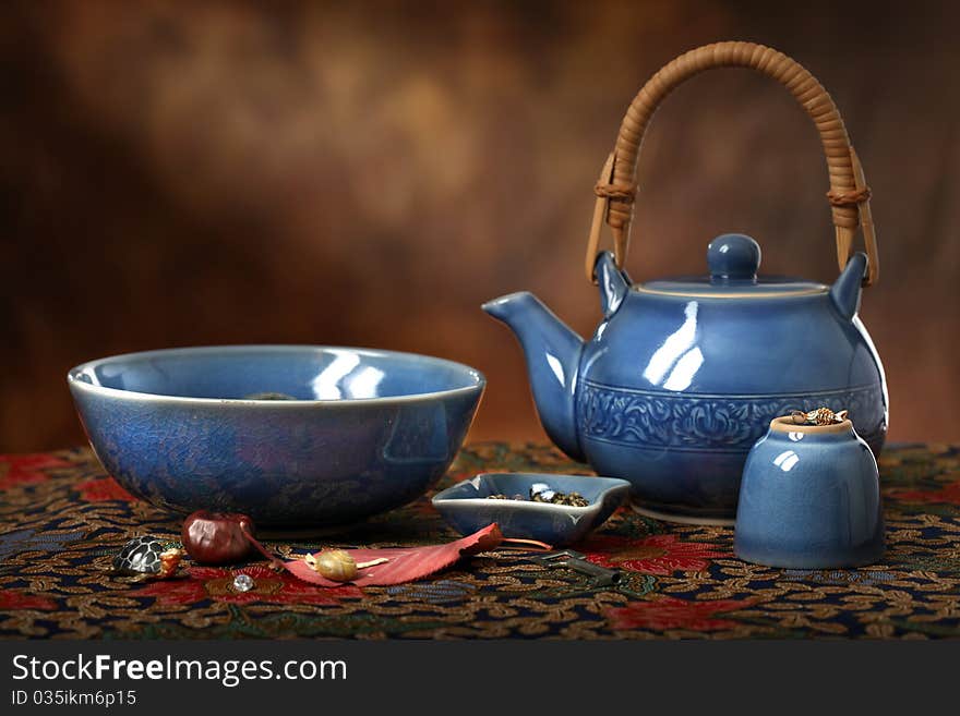 An Asian blue celedon teapot, bowl and cup along with various trinkets on a batik cloth with a sun beam in the background. An Asian blue celedon teapot, bowl and cup along with various trinkets on a batik cloth with a sun beam in the background.