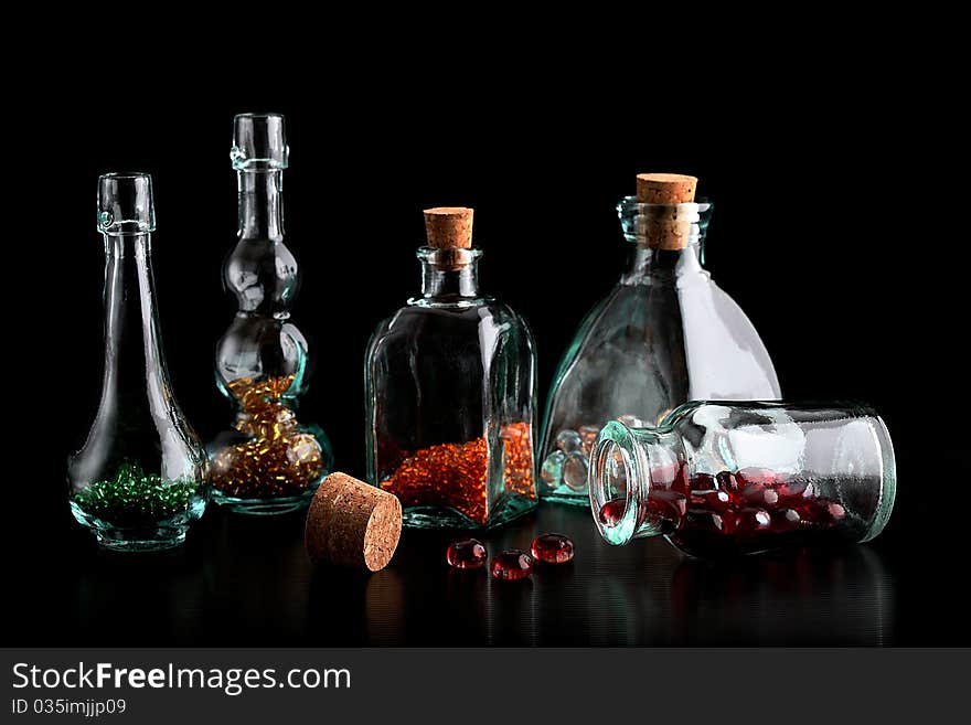 Glass bottles filled with colorful beads on a black background. Glass bottles filled with colorful beads on a black background.