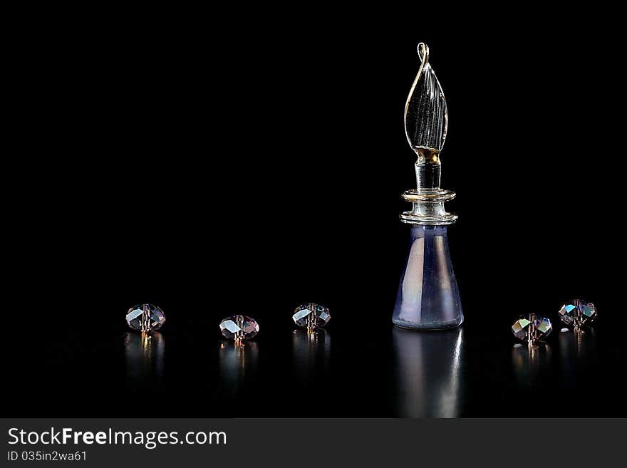 A purple perfume bottle and crystal beads on a black background. A purple perfume bottle and crystal beads on a black background.