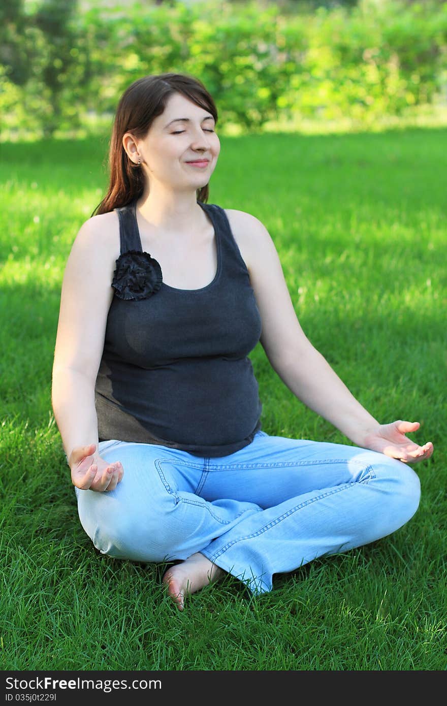 Pregnant woman sits on grass doing yoga. Pregnant woman sits on grass doing yoga