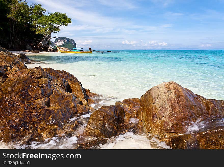 Rocks, Sea and Beach, blue skies with white fluffy clouds. Small Boat moored at the beach in the distance. Rocks, Sea and Beach, blue skies with white fluffy clouds. Small Boat moored at the beach in the distance