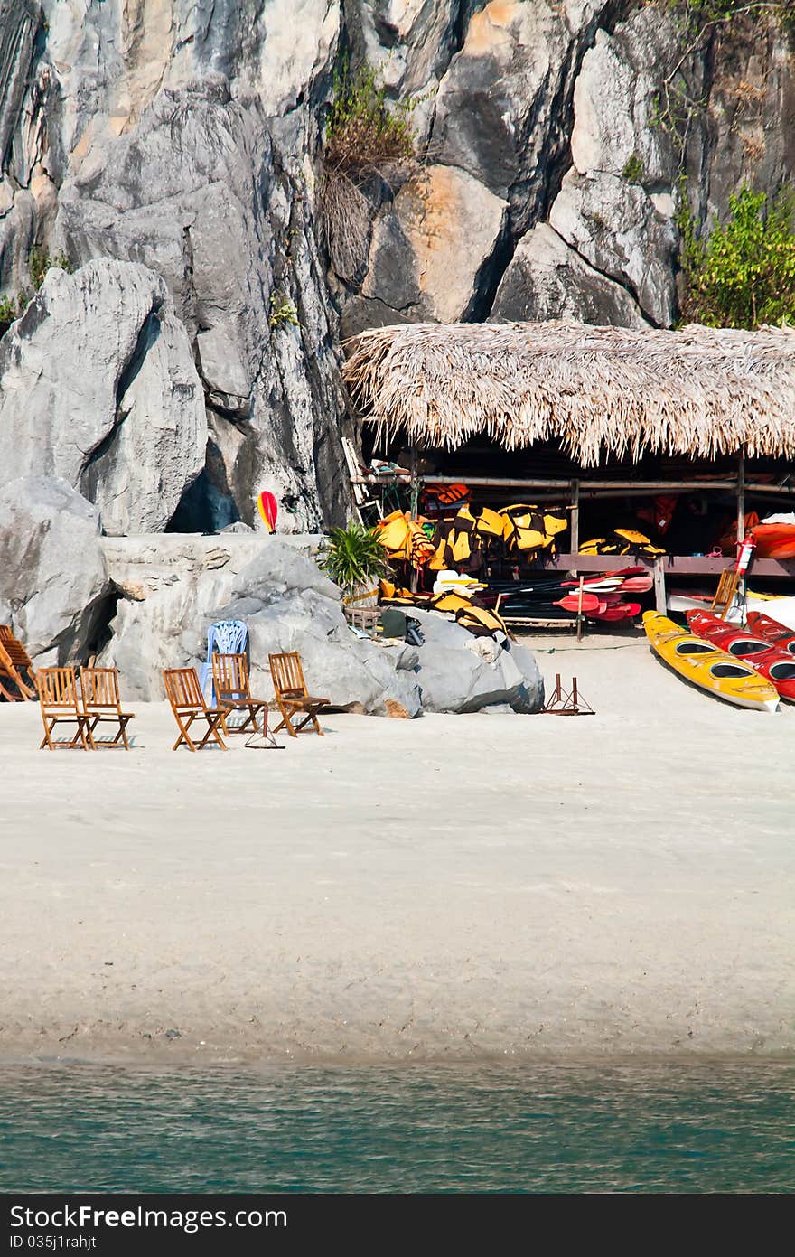 Beach and island in a remote area of Halong bay. Kayaks and deck chairs lying on the beach in the background there is a steep cliff. Beach and island in a remote area of Halong bay. Kayaks and deck chairs lying on the beach in the background there is a steep cliff