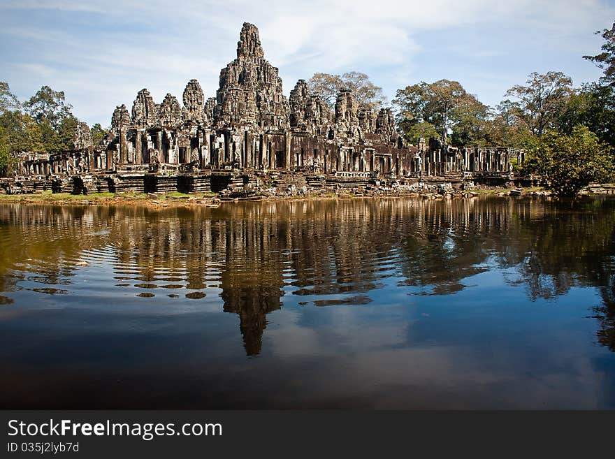 Old ruined temple near Angkor Wat. Deep blue lake in foreground with ripples and reflection of stone structure in mid ground. Old ruined temple near Angkor Wat. Deep blue lake in foreground with ripples and reflection of stone structure in mid ground