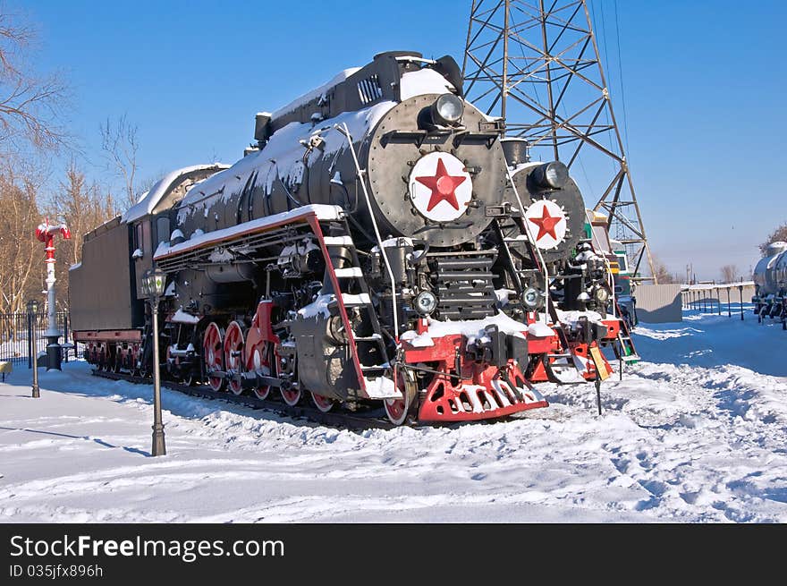 Steam locomotive beside a railway station platform. Winter. Retro train.