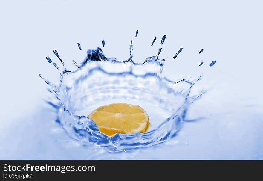 The lemon falls in water on the white-blue baclground.