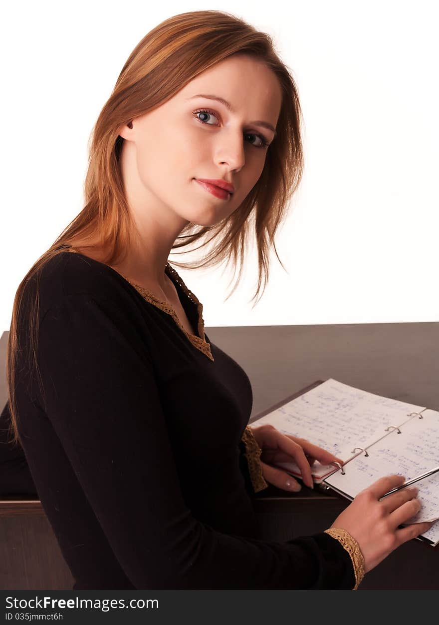 Pretty young girl sitting at the desk with her notebook open on white background