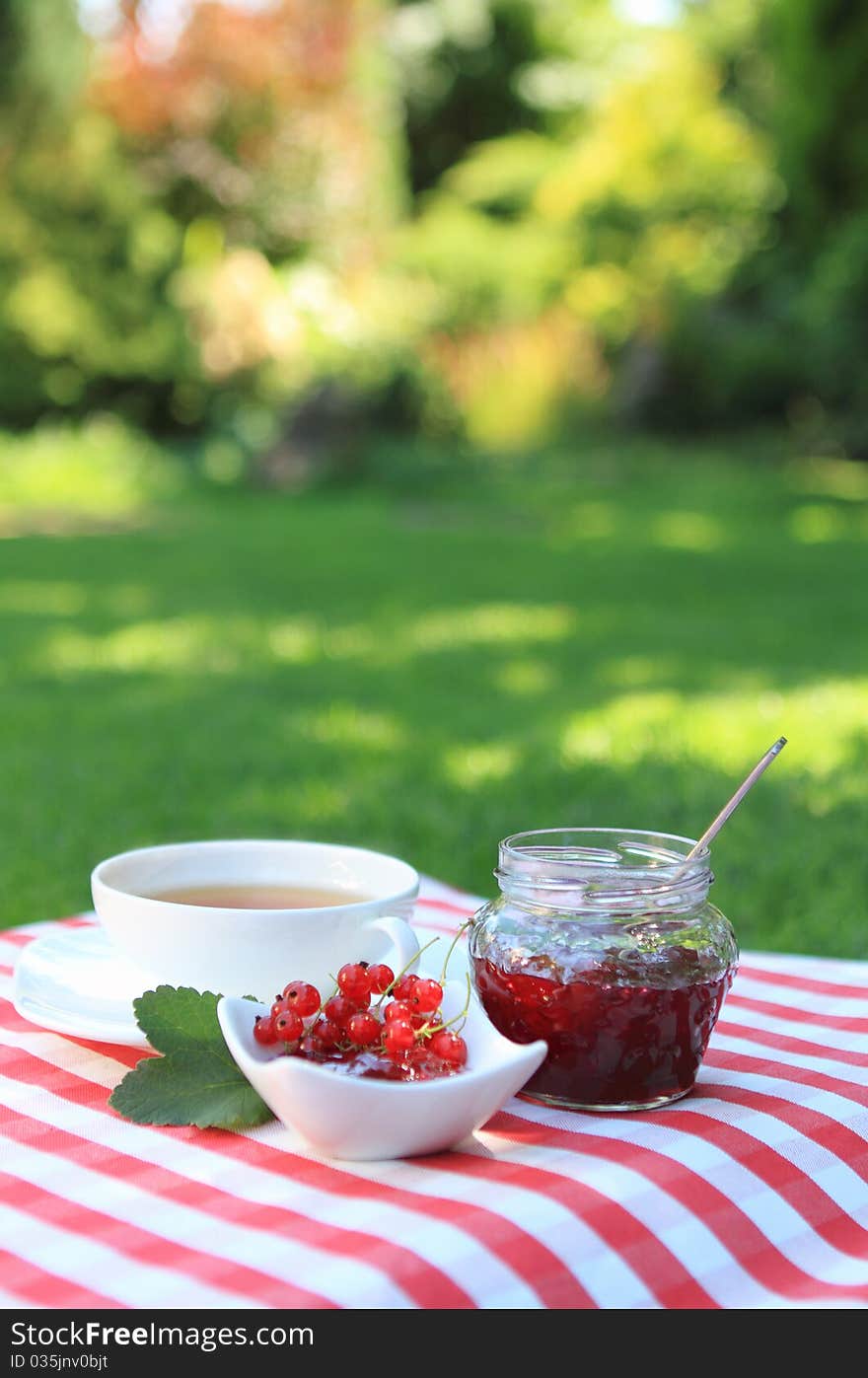 Jar of red currant jam and tea in the garden