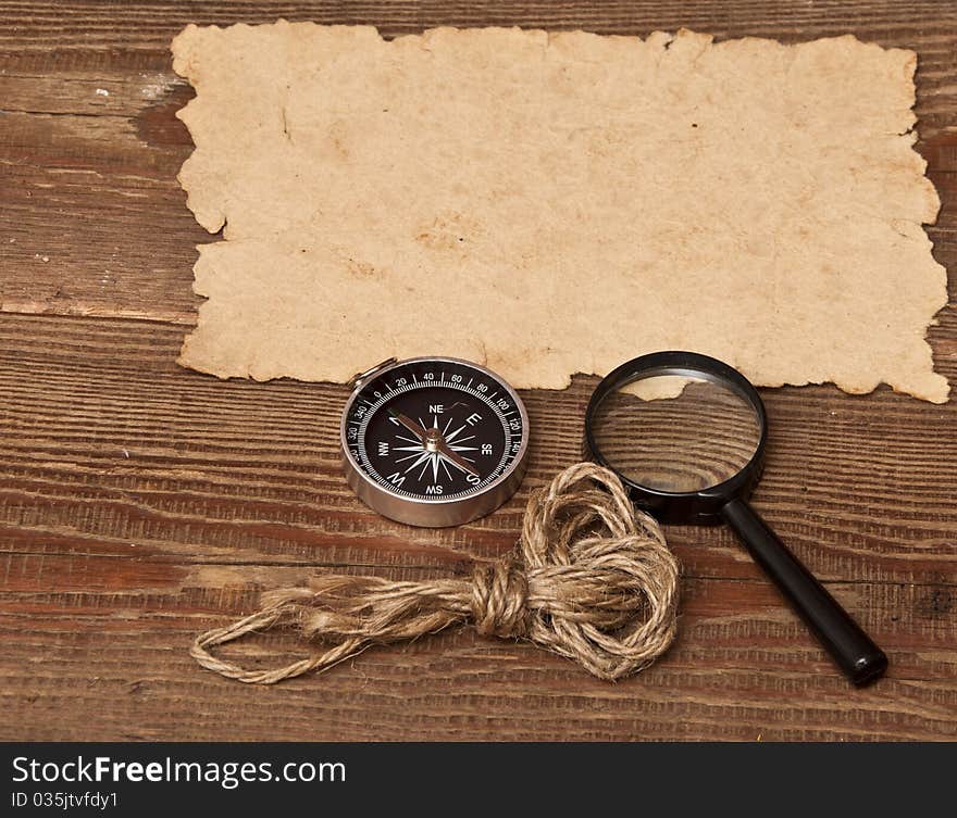 Old paper, compass and magnifying glass on wood background