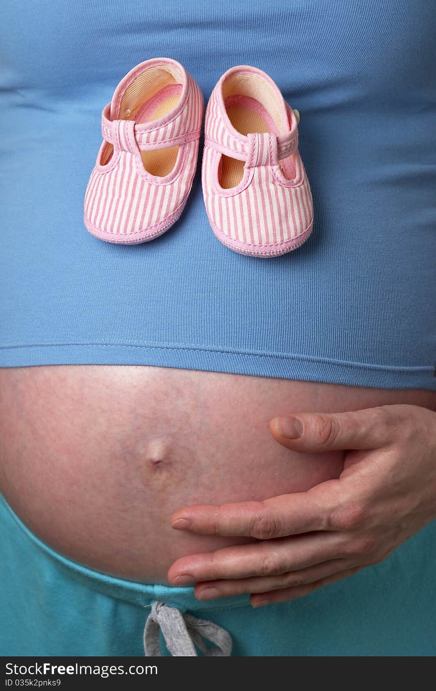 Pregnant woman profile with tiny shoes in the hands over white background. Pregnant woman profile with tiny shoes in the hands over white background