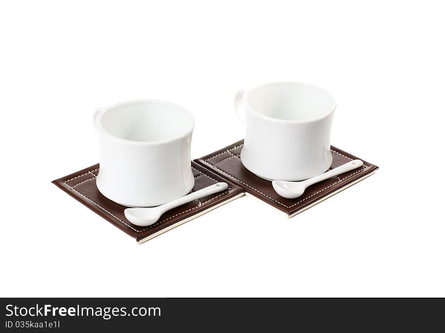 Two empty tea cups with spoons on table mats. Isolated on white background. Two empty tea cups with spoons on table mats. Isolated on white background.