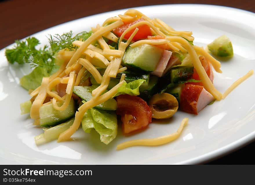 Salad with fresh vegetables and cheese, ham and olives on a plate