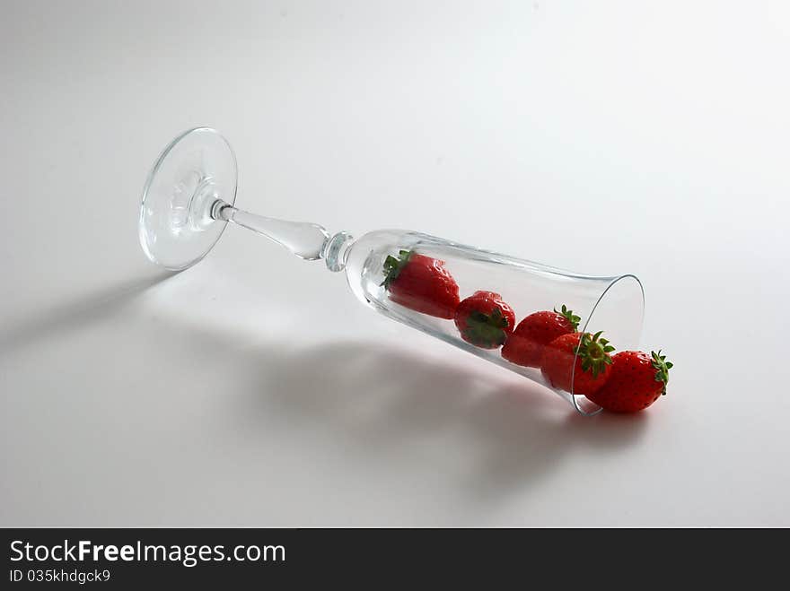 Strawberries spilled from wineglass lying on white background