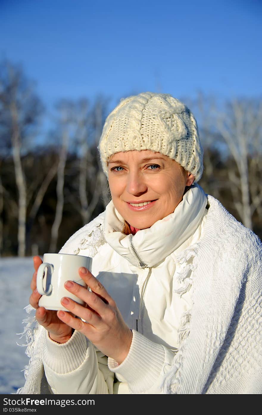 Adult woman in white, with mug in his hands  on a snowy background, bright sunny frosty day