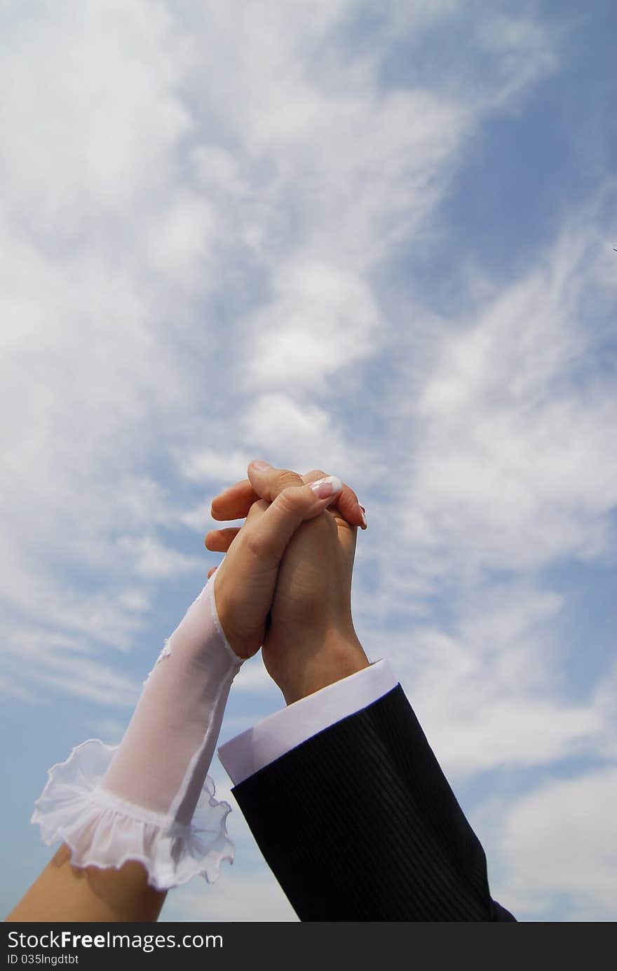 Bride and groom holding hands on sky background