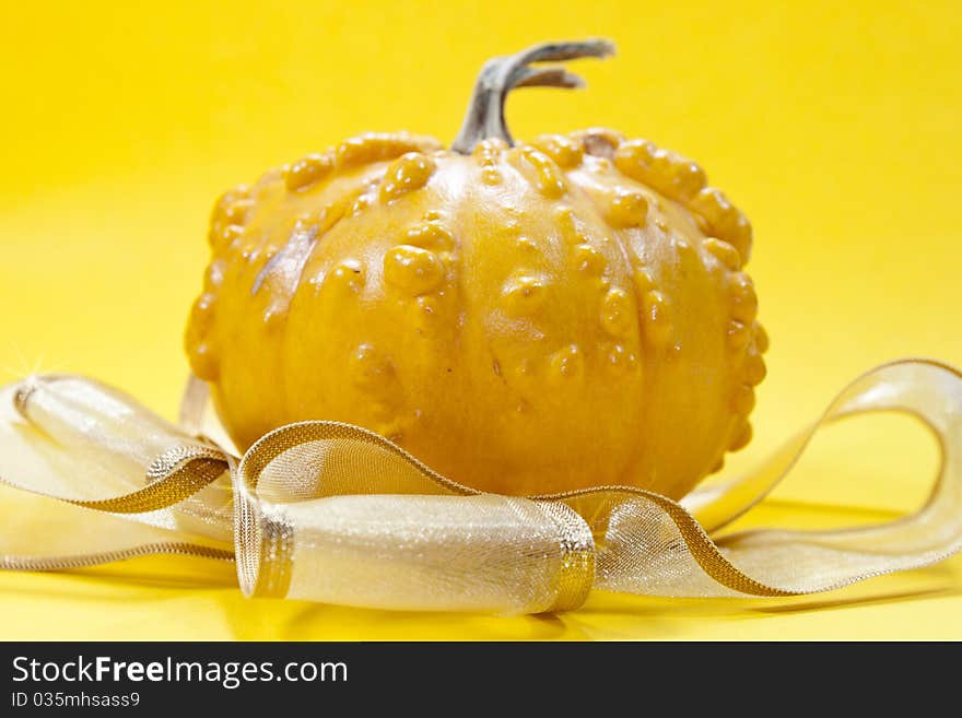 Yeallow pumpkin on yellow background with golden ribbon for hellowen or for a gift