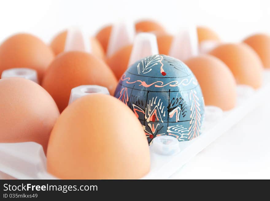 One painted Easter egg in a box with many brown chicken eggs. One painted Easter egg in a box with many brown chicken eggs