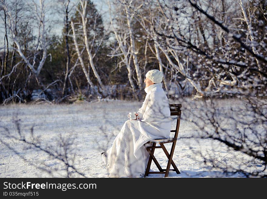 Adult woman in white, with mug in his hands on a snowy forest background, bright sunny frosty day. Adult woman in white, with mug in his hands on a snowy forest background, bright sunny frosty day