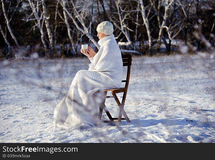 Adult woman in white, with mug in his hands  on a snowy forest background, bright sunny frosty day. Adult woman in white, with mug in his hands  on a snowy forest background, bright sunny frosty day.