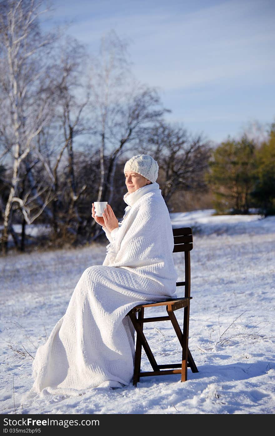 Adult woman in white, with mug in his hands  on a snowy forest background, bright sunny frosty day. Adult woman in white, with mug in his hands  on a snowy forest background, bright sunny frosty day.