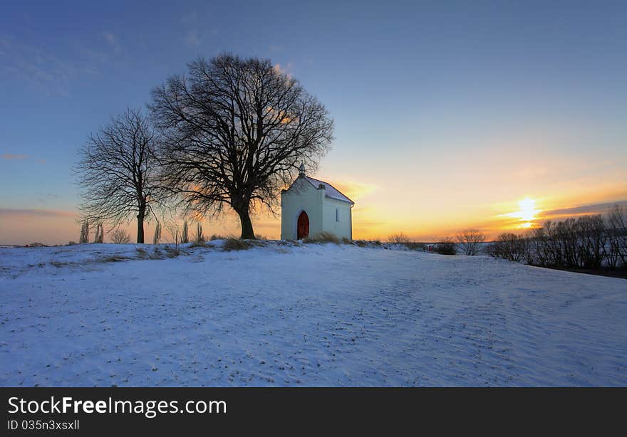 Sunset on frozen field with a chapel and clouds