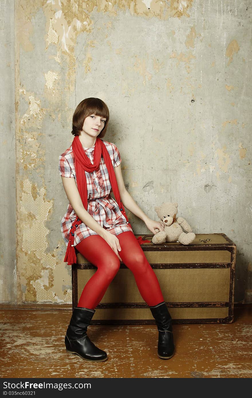 Young attractive woman in the background of the old concrete wall sits on an old suitcase sitting next to a soft toy Teddy. Young attractive woman in the background of the old concrete wall sits on an old suitcase sitting next to a soft toy Teddy