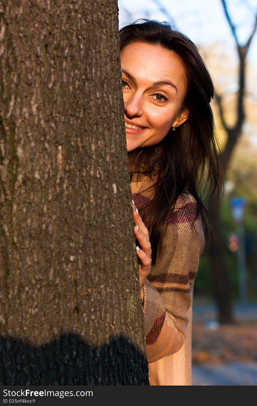 Beautiful young woman looking out behind the tree in autumn. Beautiful young woman looking out behind the tree in autumn