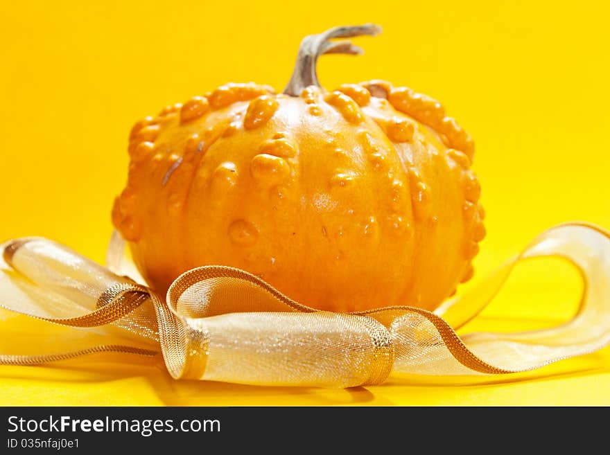 Yeallow pumpkin on yellow background with golden ribbon for hellowen or for a gift