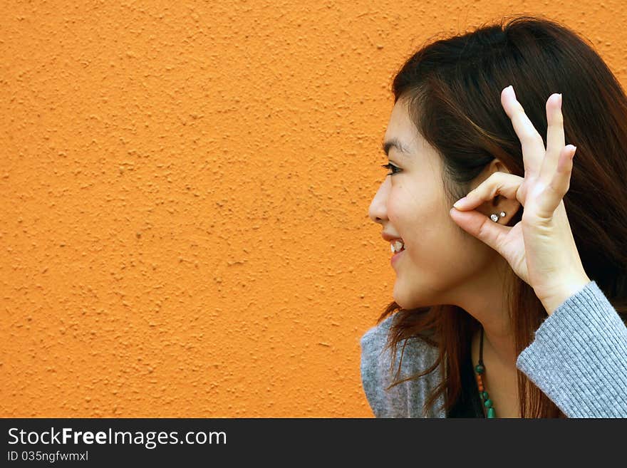 She is an Asian and trying to use her hands to pretend listening to the others. It was taken in an orange background. She is an Asian and trying to use her hands to pretend listening to the others. It was taken in an orange background.