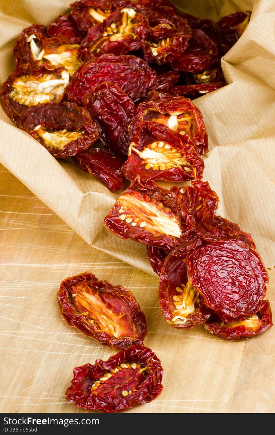 Ripe red sun-dried plum tomatoes spilling out of a brown recycled brown paper shopping bag onto a wooden cutting board surface. Ripe red sun-dried plum tomatoes spilling out of a brown recycled brown paper shopping bag onto a wooden cutting board surface