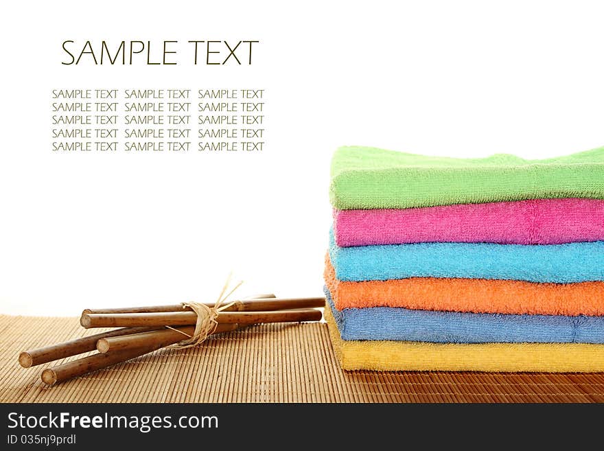 Lots of colorful bath towels stacked on each other. Side by side on a wooden surface lie bamboo sticks. Isolated