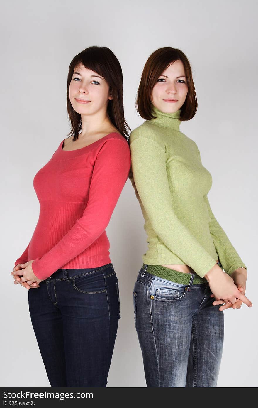 Two young brunette girls in red and green shirts standing back to back. Two young brunette girls in red and green shirts standing back to back