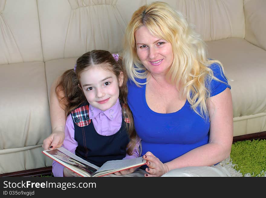 Portrait of a little school girl and her mother reading froam a book and looking at the camera. Portrait of a little school girl and her mother reading froam a book and looking at the camera.