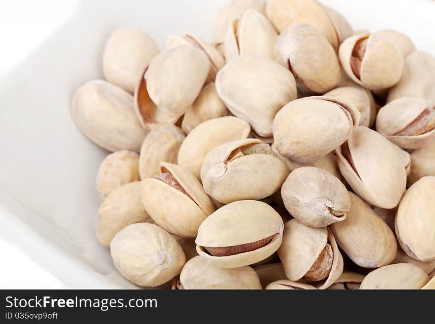 Many pistachios lie on a white plate, the Shot horizontal, focus in the shot center, a background white