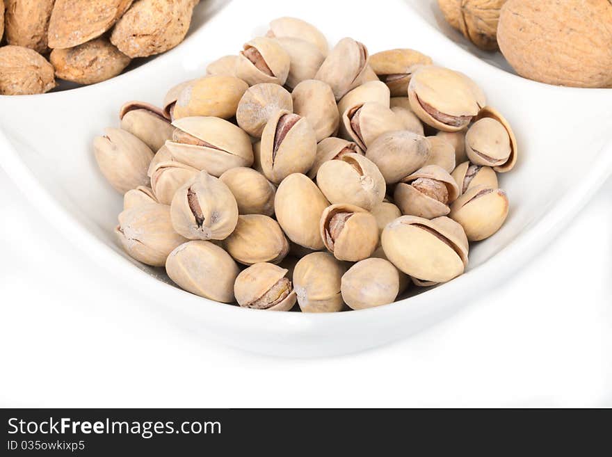 Many pistachios lie on a white plate, the Shot horizontal, focus in the shot center, a background white