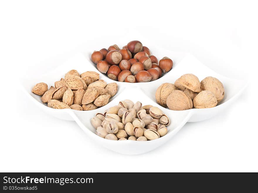 Four kinds of popular nuts lie separately in a white plate on a white background. A shot horizontal, focus in the shot center