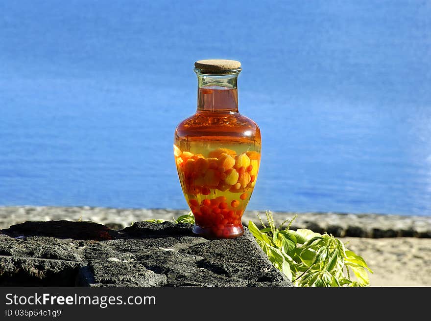 A glass jar containing tropical fruits steeping in rhum (made from sugar cane juice), standing on a rock with the sea in the background. A glass jar containing tropical fruits steeping in rhum (made from sugar cane juice), standing on a rock with the sea in the background.