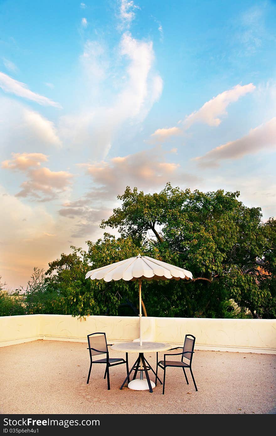 A rooftop getaway, with a table, umbrella and two chairs.  A beautiful sky and clouds are in the background. A rooftop getaway, with a table, umbrella and two chairs.  A beautiful sky and clouds are in the background.