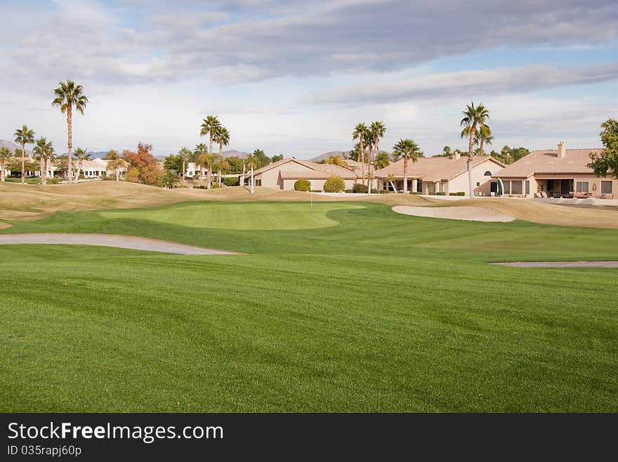 A golf course green on a cloudy day with palm trees and houses in the background. A golf course green on a cloudy day with palm trees and houses in the background.